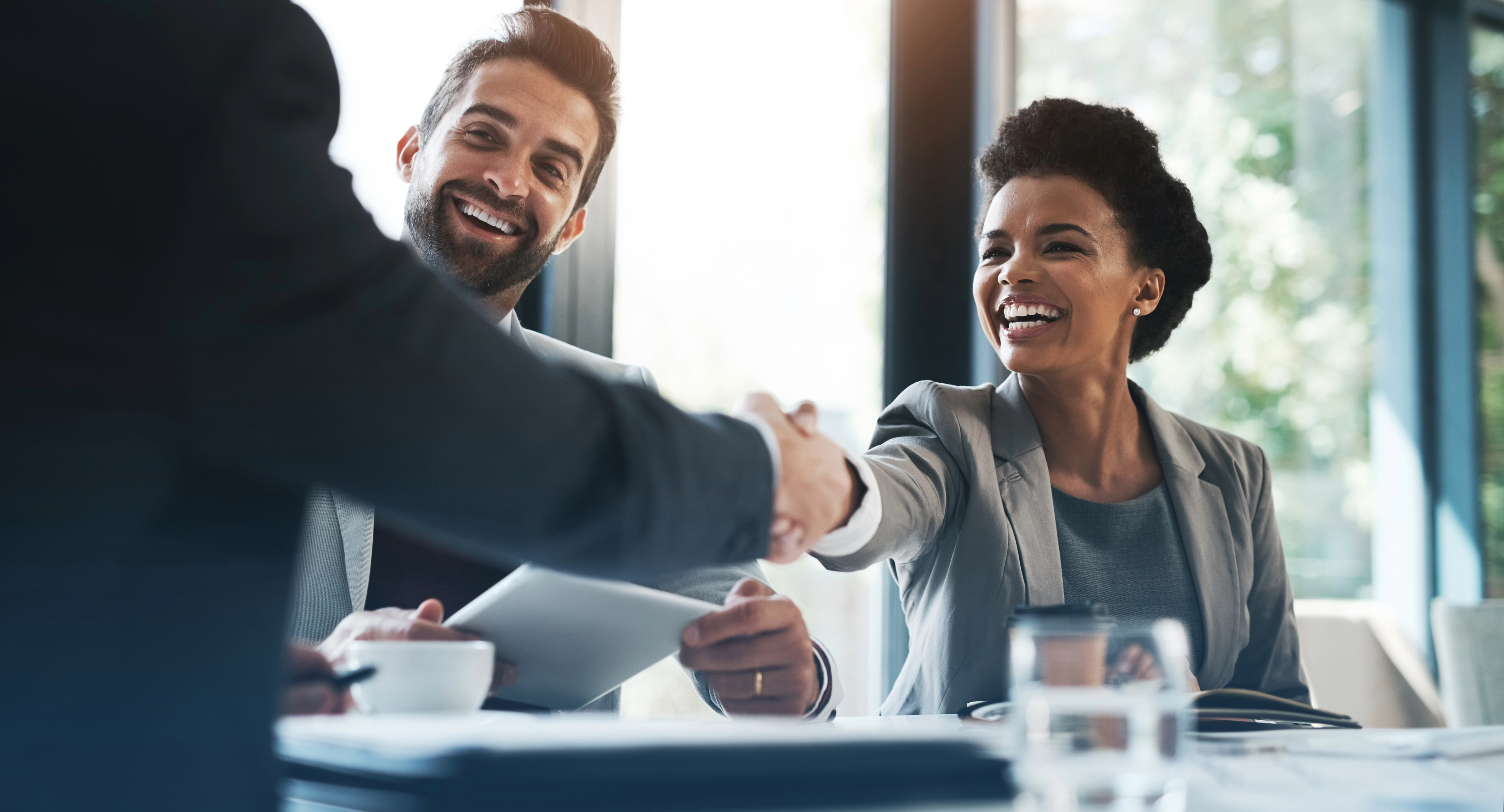 person shaking hands with another while coworker stands by and holds contract.
